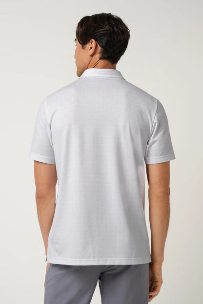 A man viewed from the back wearing a light gray short-sleeve polo shirt and gray trousers, standing against a plain light gray studio background.