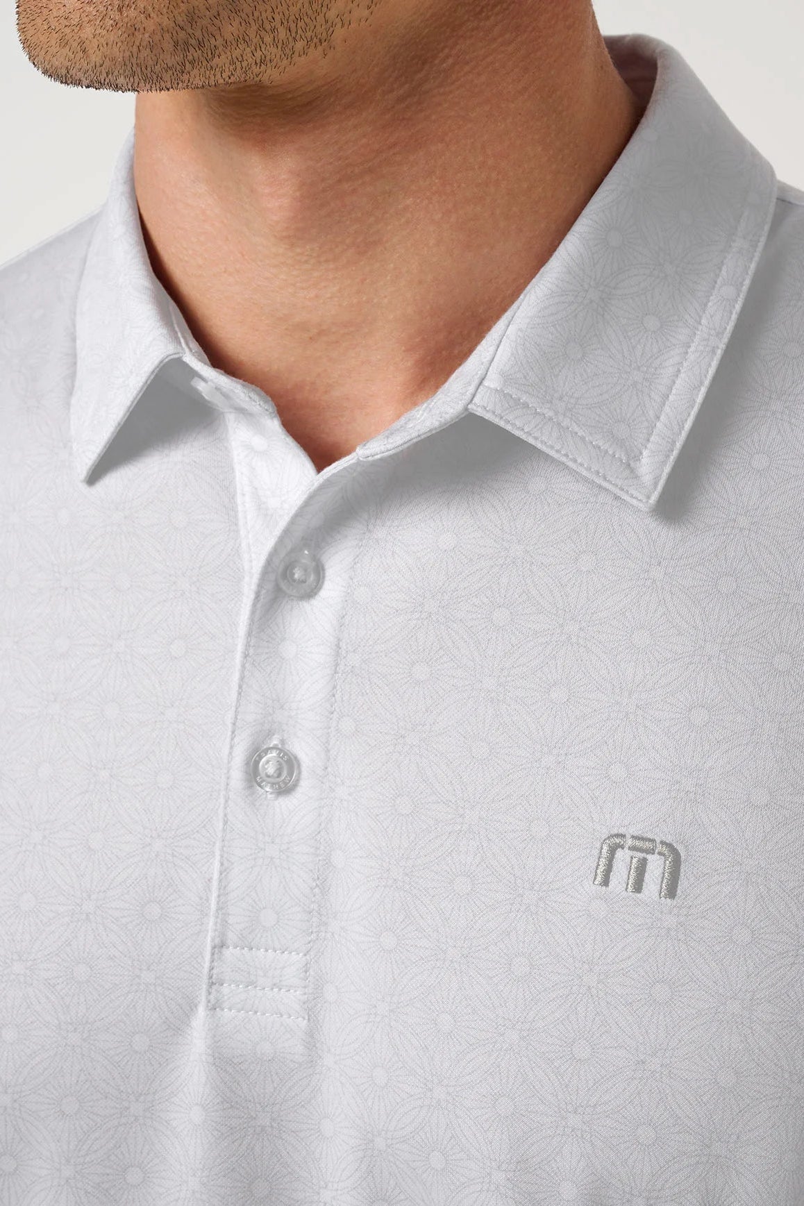 Close-up of a light gray polo shirt with a logo on a neutral background