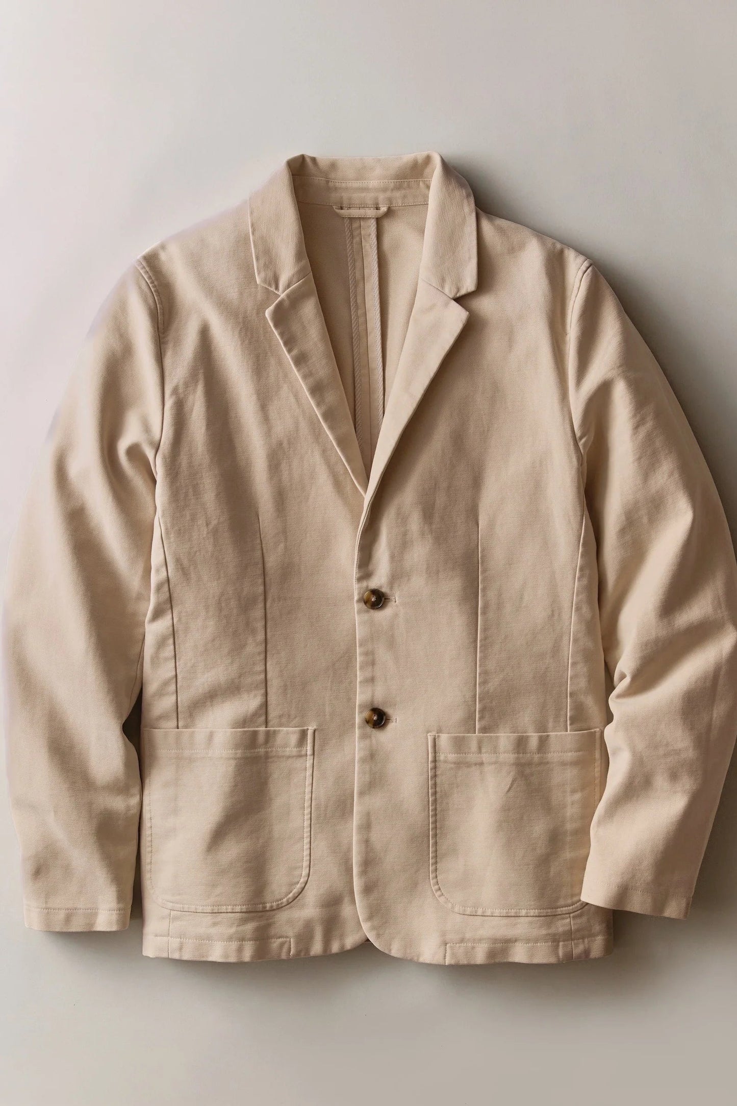 A light beige linen-blend blazer jacket with notch lapels, a two-button front closure, and two large front patch pockets, laid flat against a neutral light gray background.
