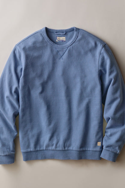A dusty blue crewneck sweatshirt laid flat against a neutral beige background.
