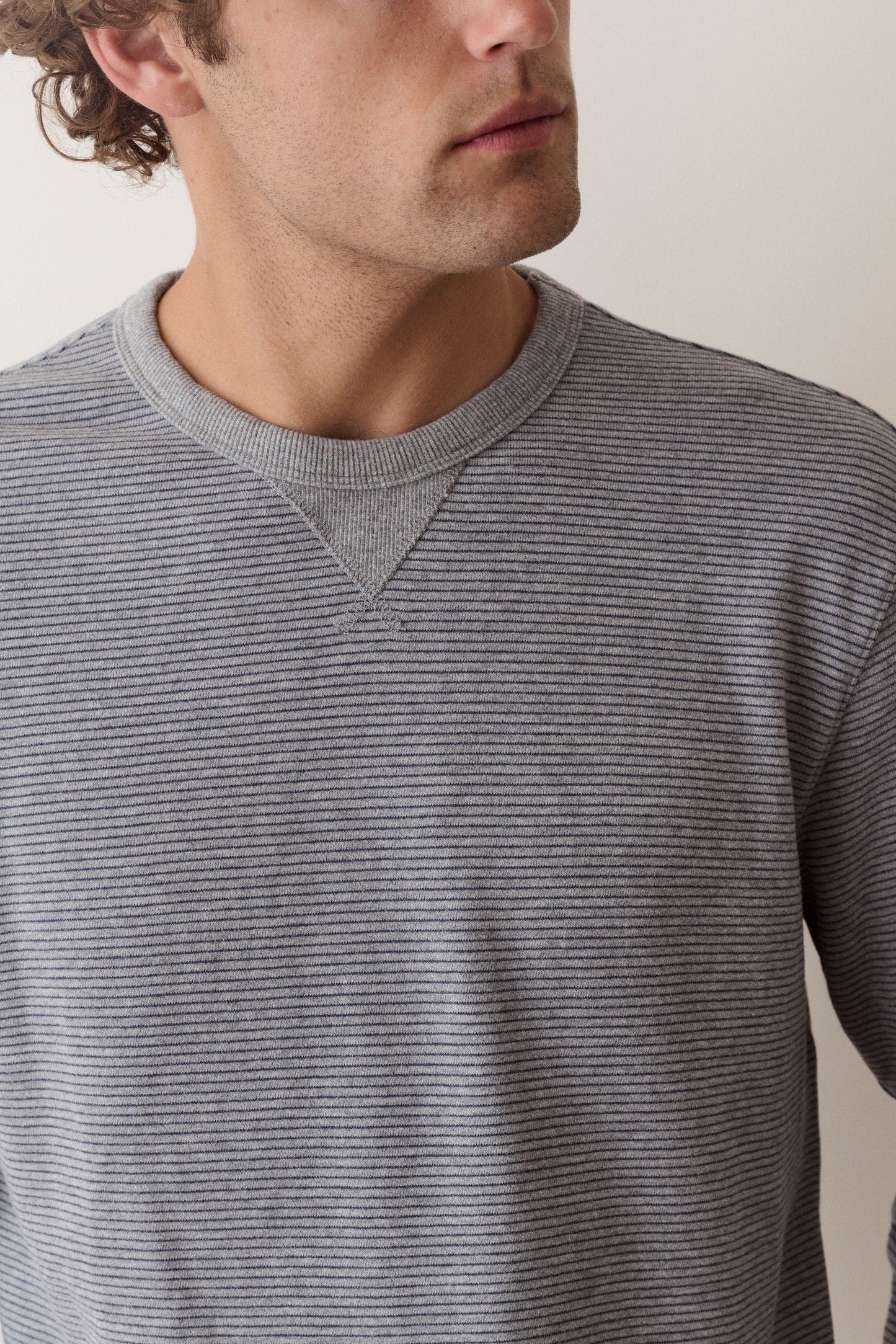 A close-up of a man wearing a gray and black horizontally striped long-sleeve crewneck sweater, cropped from the side of his face to the chest.