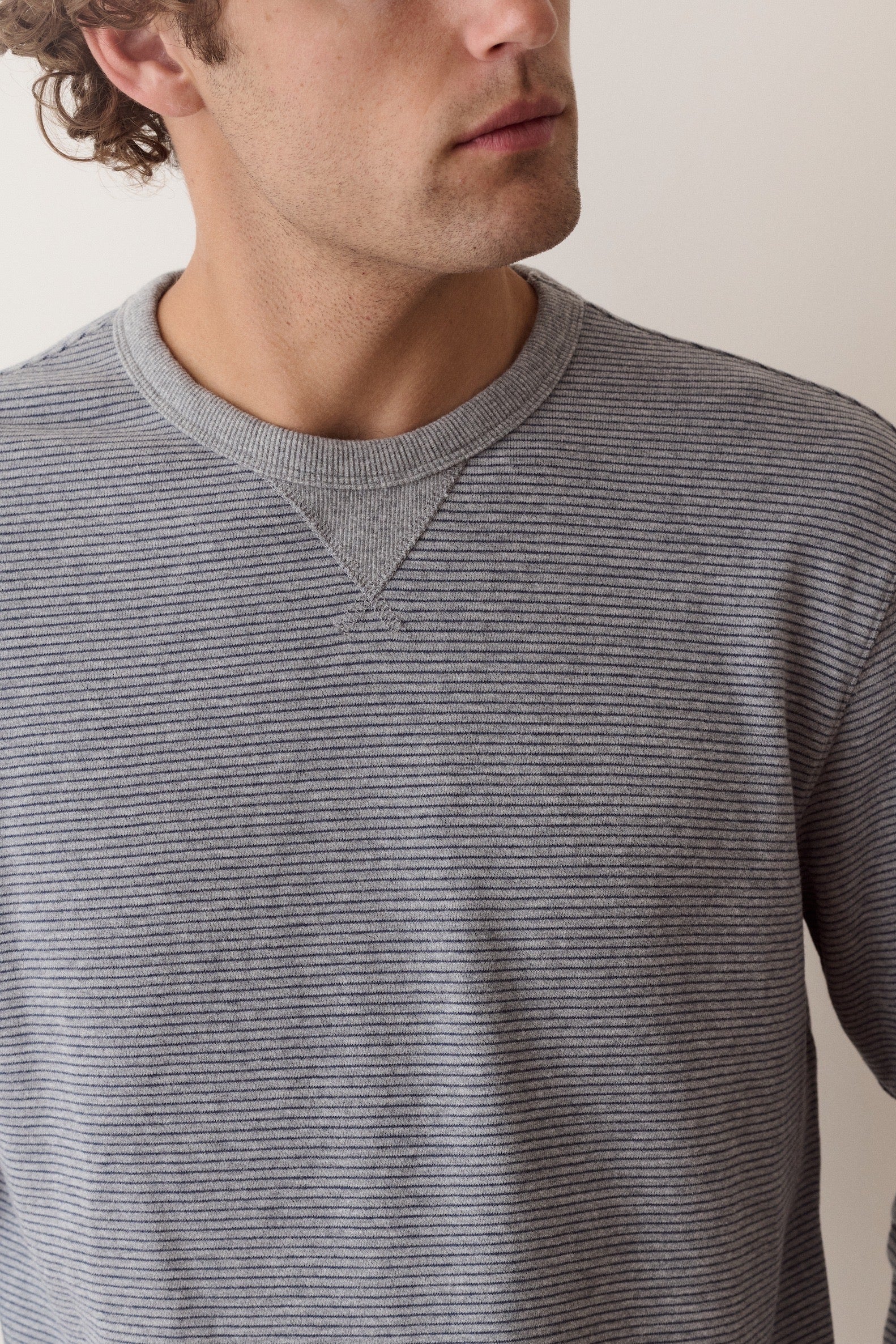 A close-up of a man wearing a gray and black horizontally striped long-sleeve crewneck sweater, cropped from the side of his face to the chest.