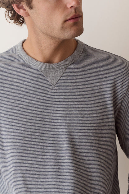 A close-up of a man wearing a gray and black horizontally striped long-sleeve crewneck sweater, cropped from the side of his face to the chest.