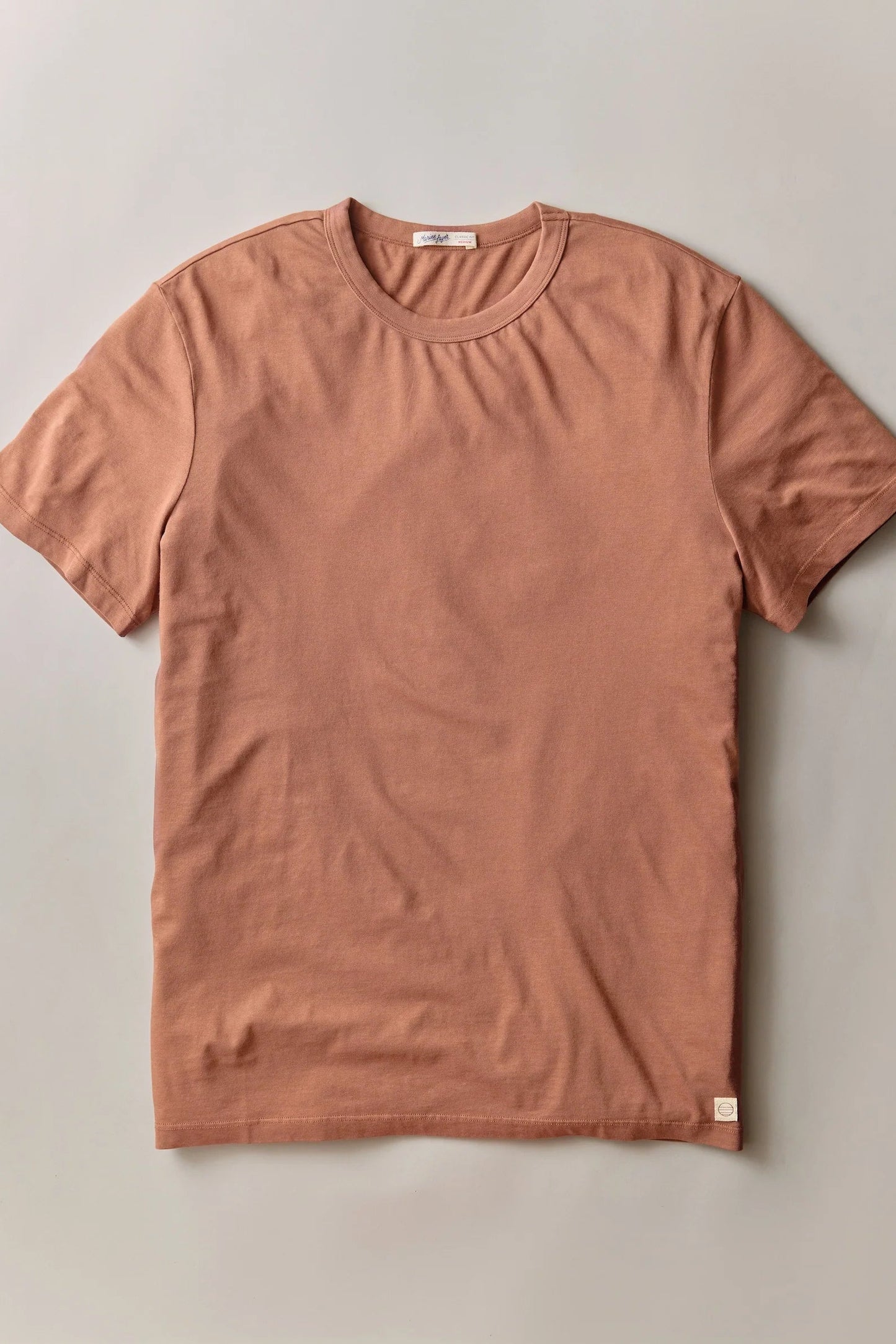 A short-sleeve crewneck t-shirt in a muted terracotta or dusty rose color, laid flat against a neutral light gray background.
