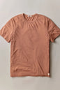 A short-sleeve crewneck t-shirt in a muted terracotta or dusty rose color, laid flat against a neutral light gray background.
