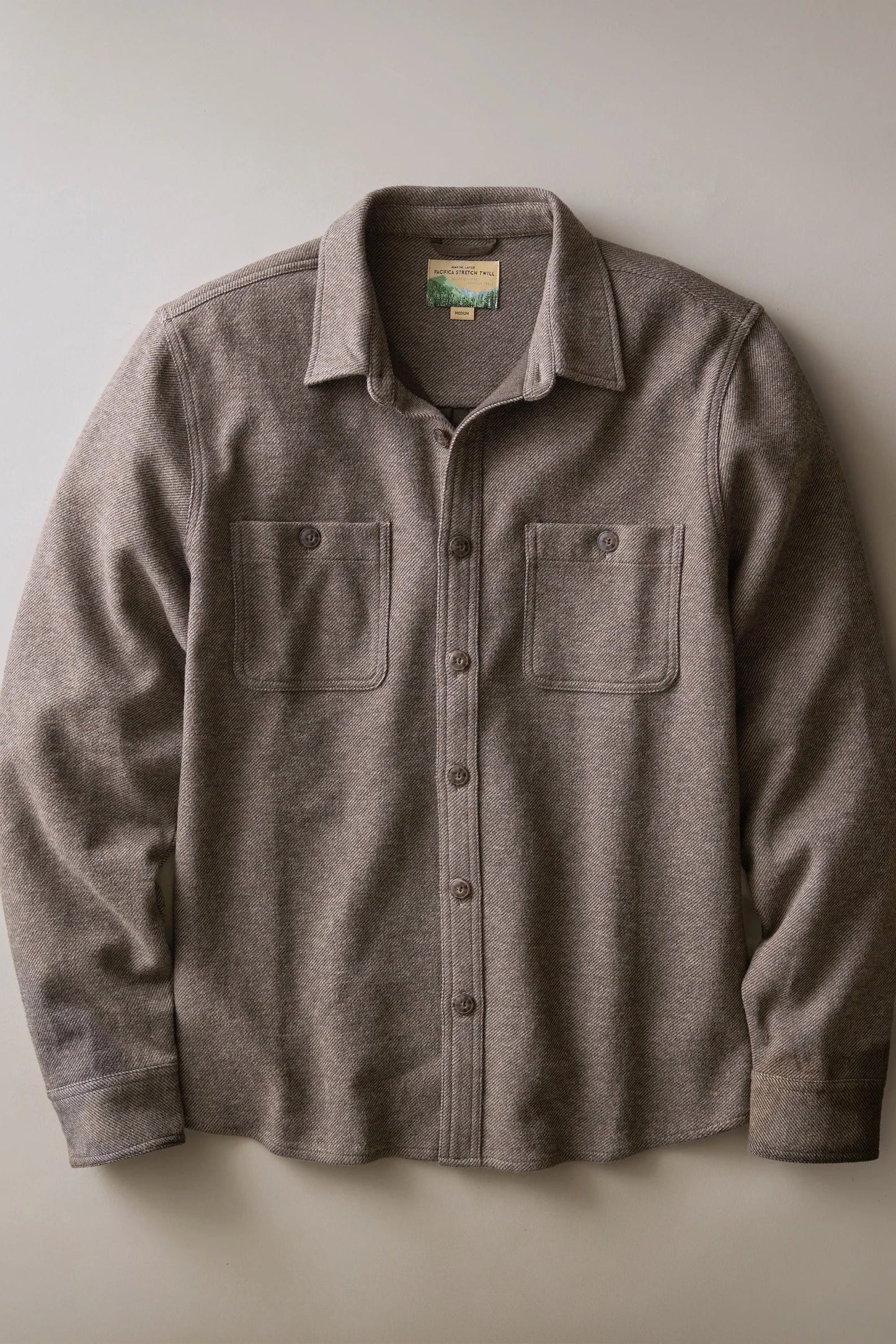 A long-sleeve button-up shirt jacket in a heathered taupe-brown fabric, featuring two buttoned chest pockets and a classic collar, laid flat against a neutral light gray background.