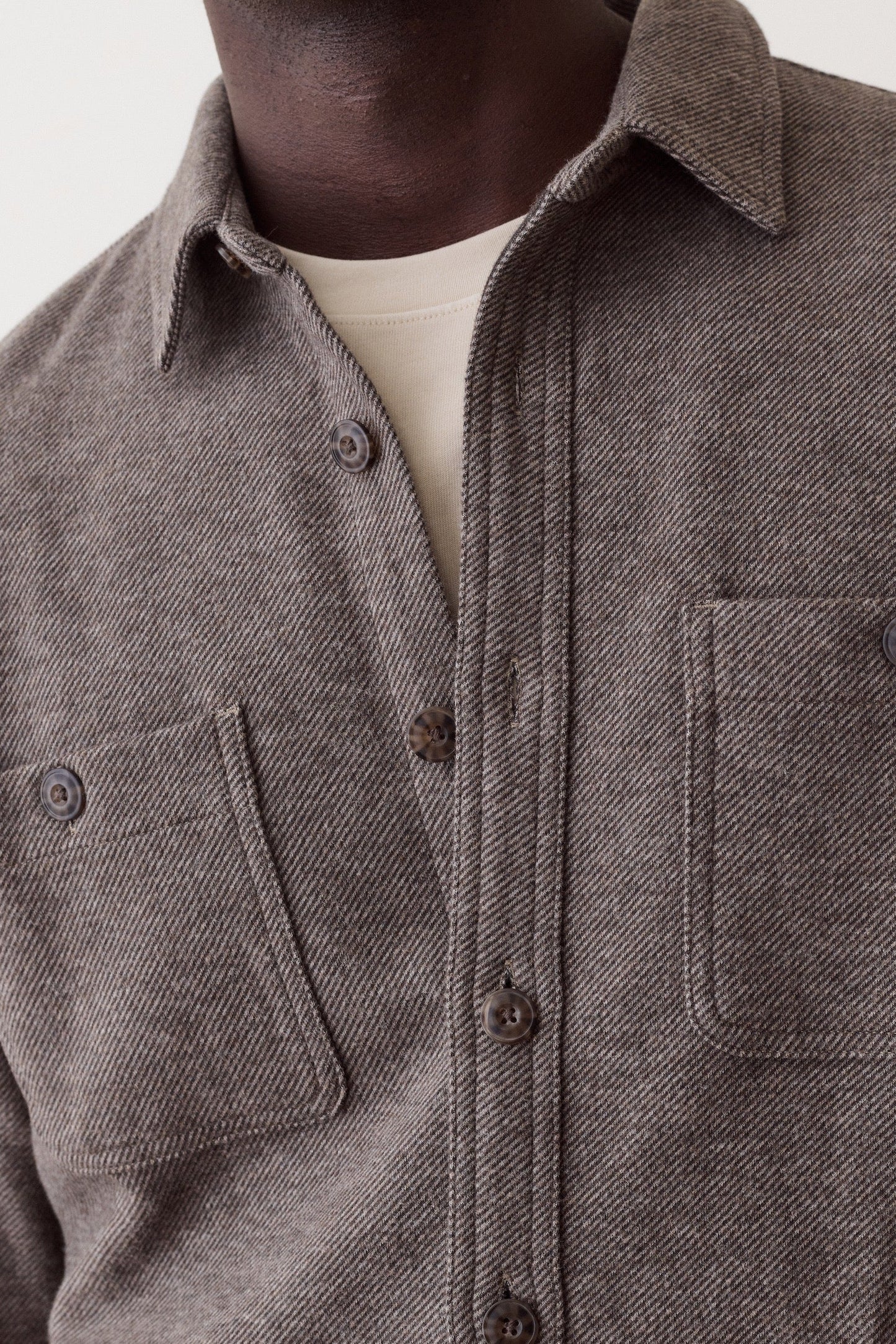 Close-up of a person wearing a textured charcoal gray button-up shirt with two chest pockets over a cream undershirt, against a plain light background.
