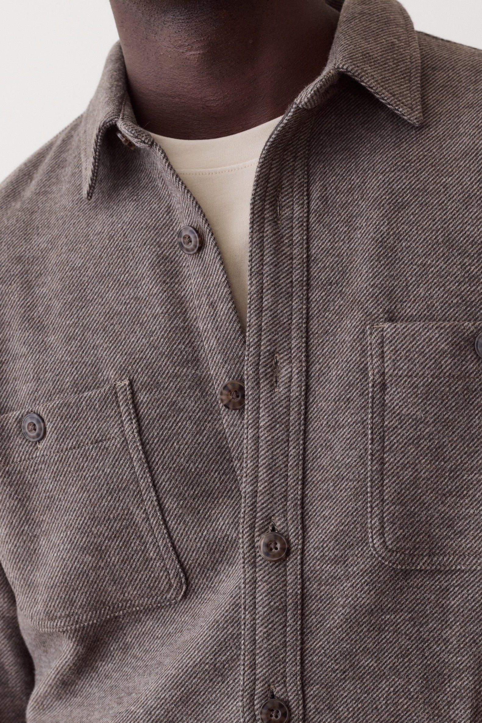Close-up of a person wearing a textured charcoal gray button-up shirt with two chest pockets over a cream undershirt, against a plain light background.
