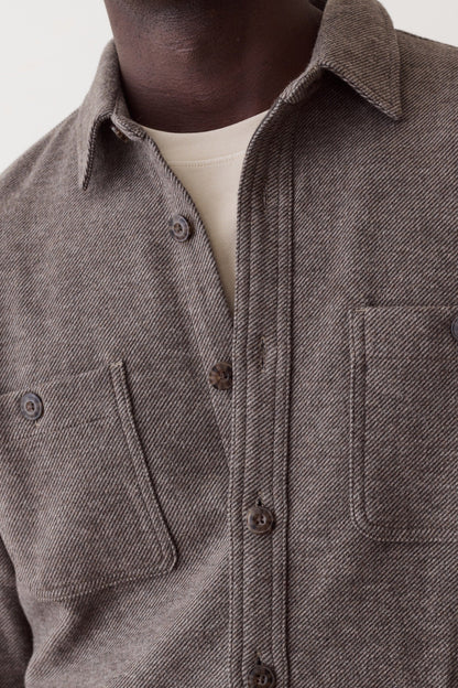 Close-up of a person wearing a textured charcoal gray button-up shirt with two chest pockets over a cream undershirt, against a plain light background.