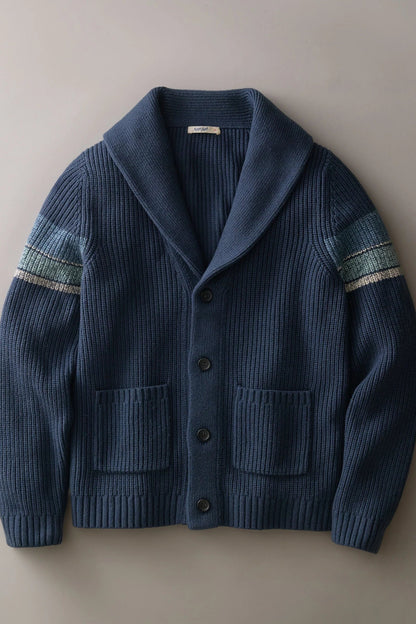 A dark blue ribbed knit cardigan sweater with a shawl collar, front buttons, and two front pockets, featuring striped knit detailing on the upper sleeves, laid flat against a neutral gray background.