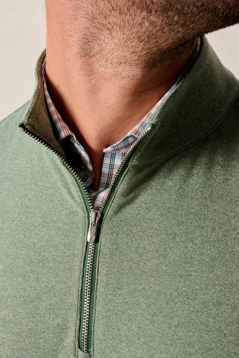 Close-up of a man wearing a sage green quarter-zip pullover sweater layered over a plaid collared shirt, showing the collar and zipper area.