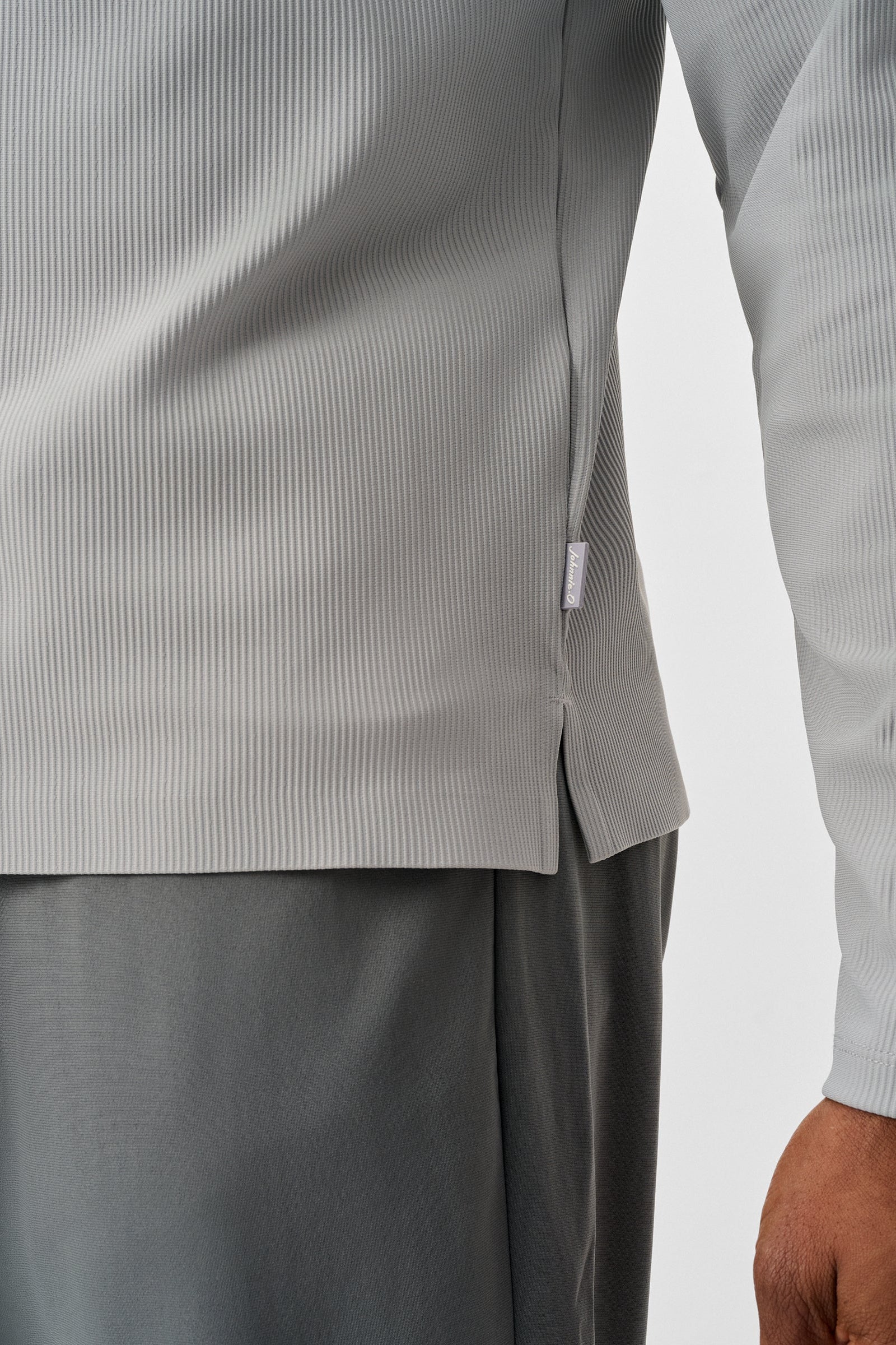 Close-up of a person wearing a light gray long-sleeve shirt and dark gray pants on a white background.