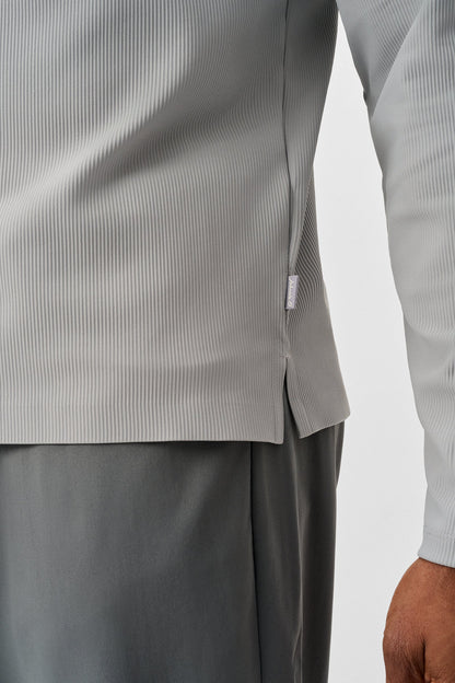 Close-up of a person wearing a light gray long-sleeve shirt and dark gray pants on a white background.