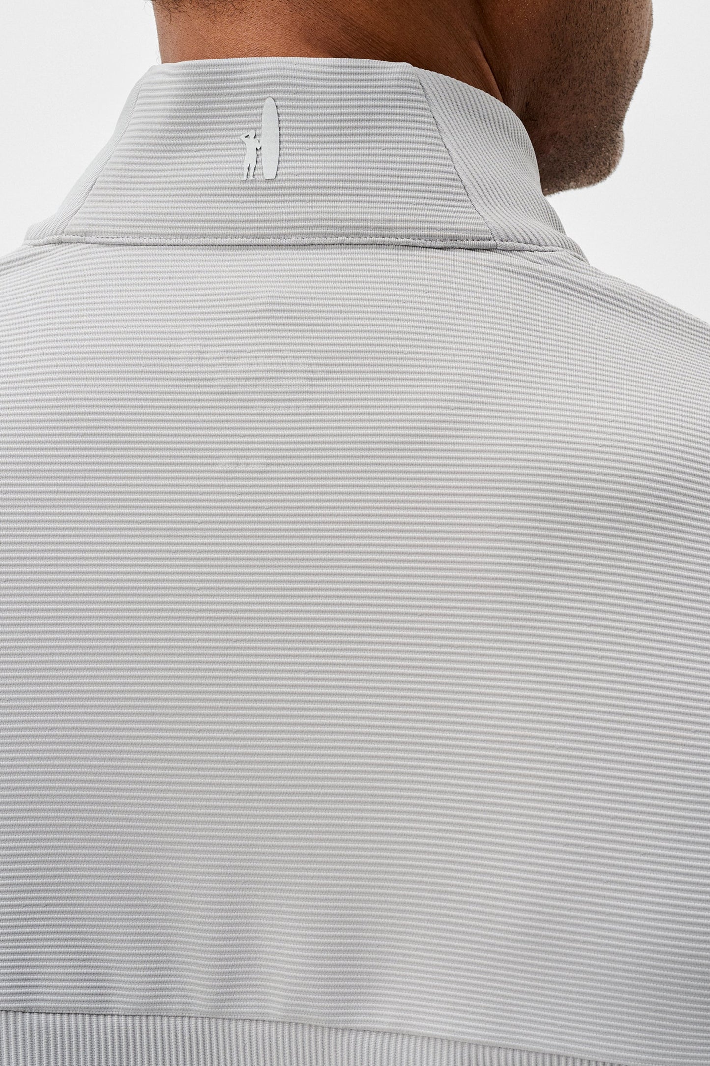 Close-up of a light gray ribbed knit sweater with a brand logo on a white background