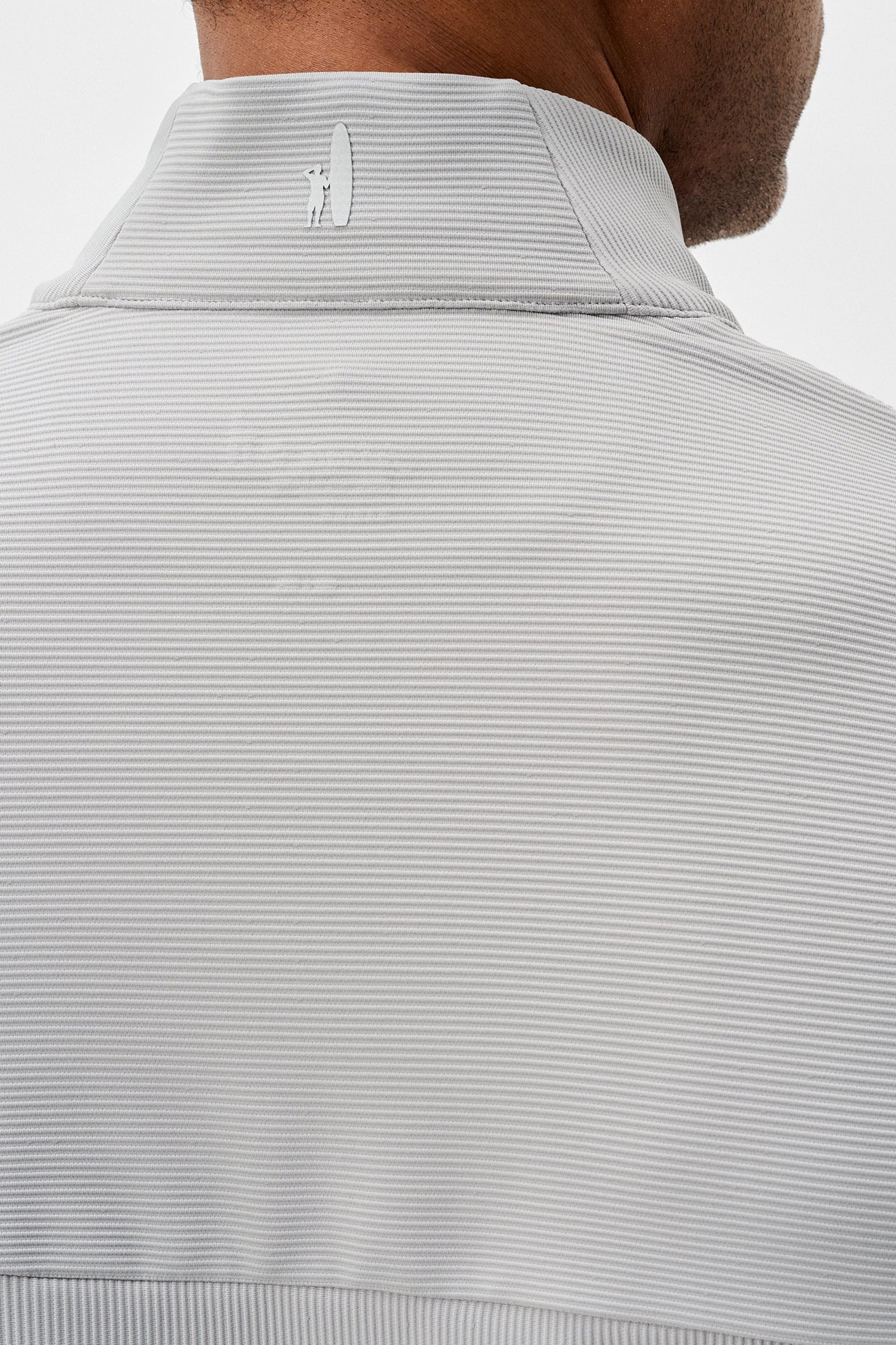 Close-up of a light gray ribbed knit sweater with a brand logo on a white background