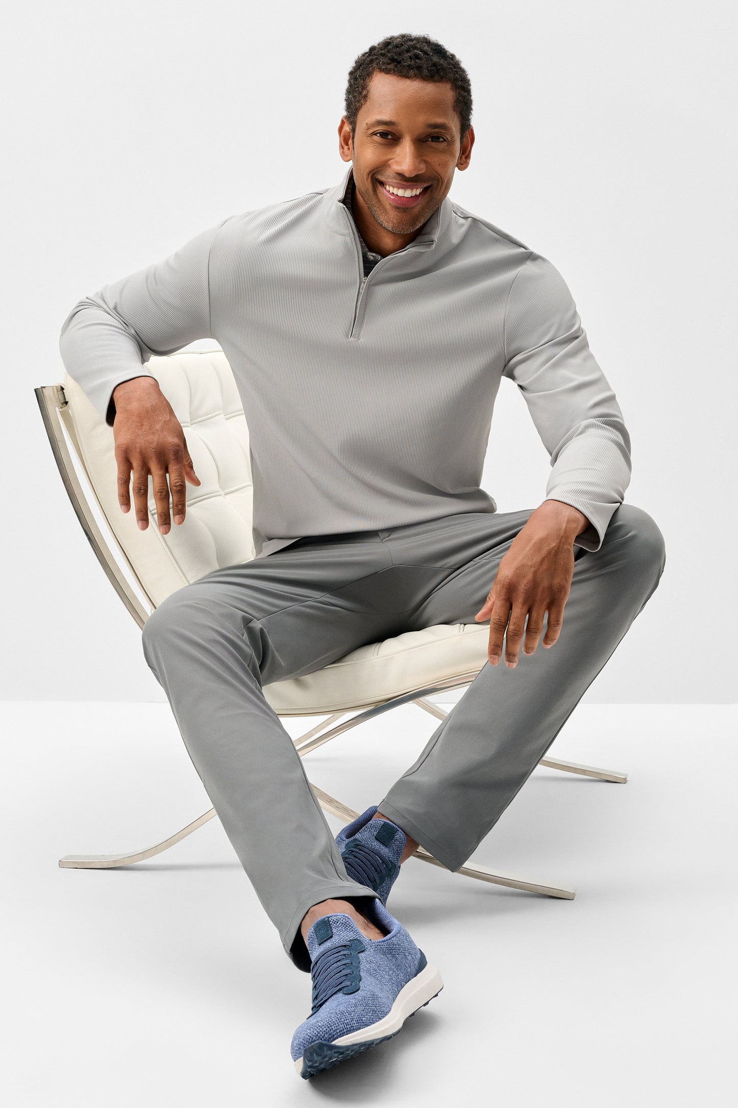 Man sitting on a chair wearing a gray outfit with blue socks on a white background
