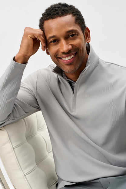Man wearing a light gray pullover sitting on a white chair against a plain background