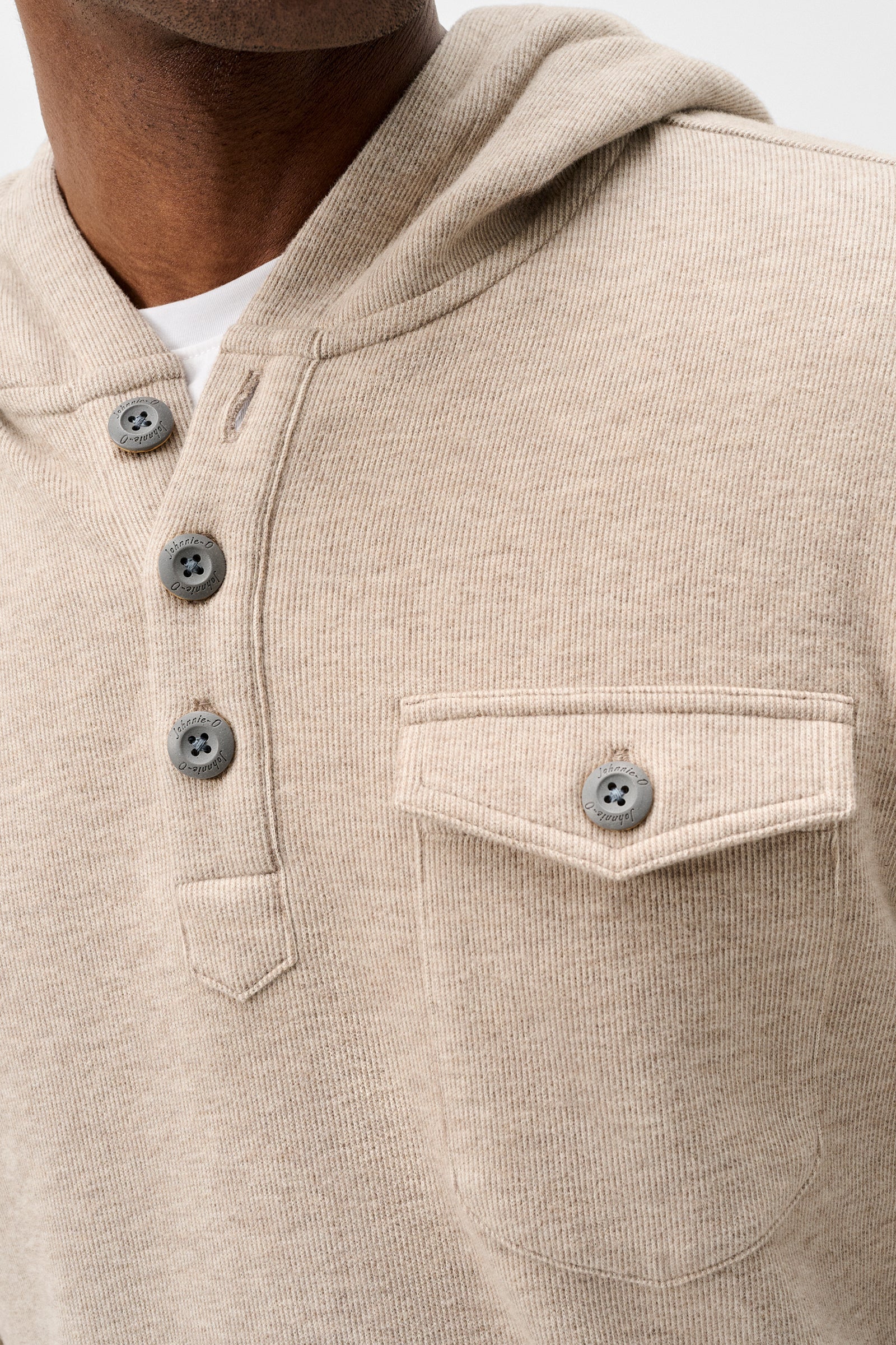 Close-up of a beige ribbed knit hooded pullover sweater with a three-button henley neckline and a chest pocket, worn by a model.