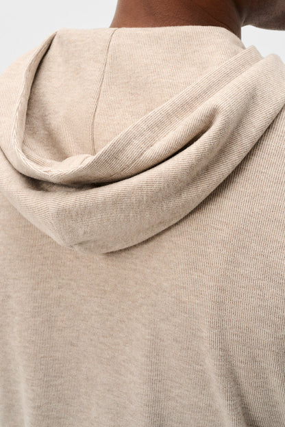 Close-up of a person wearing a light beige hooded sweatshirt, showing the back of the neck, shoulders, and the draped hood against a plain light background.