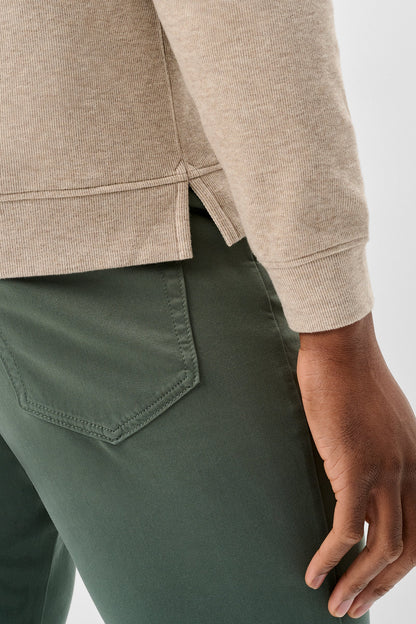 Close-up of a person wearing a light beige knit top and dark green pants, showing the side seam detail and back pocket of the trousers against a light gray background.