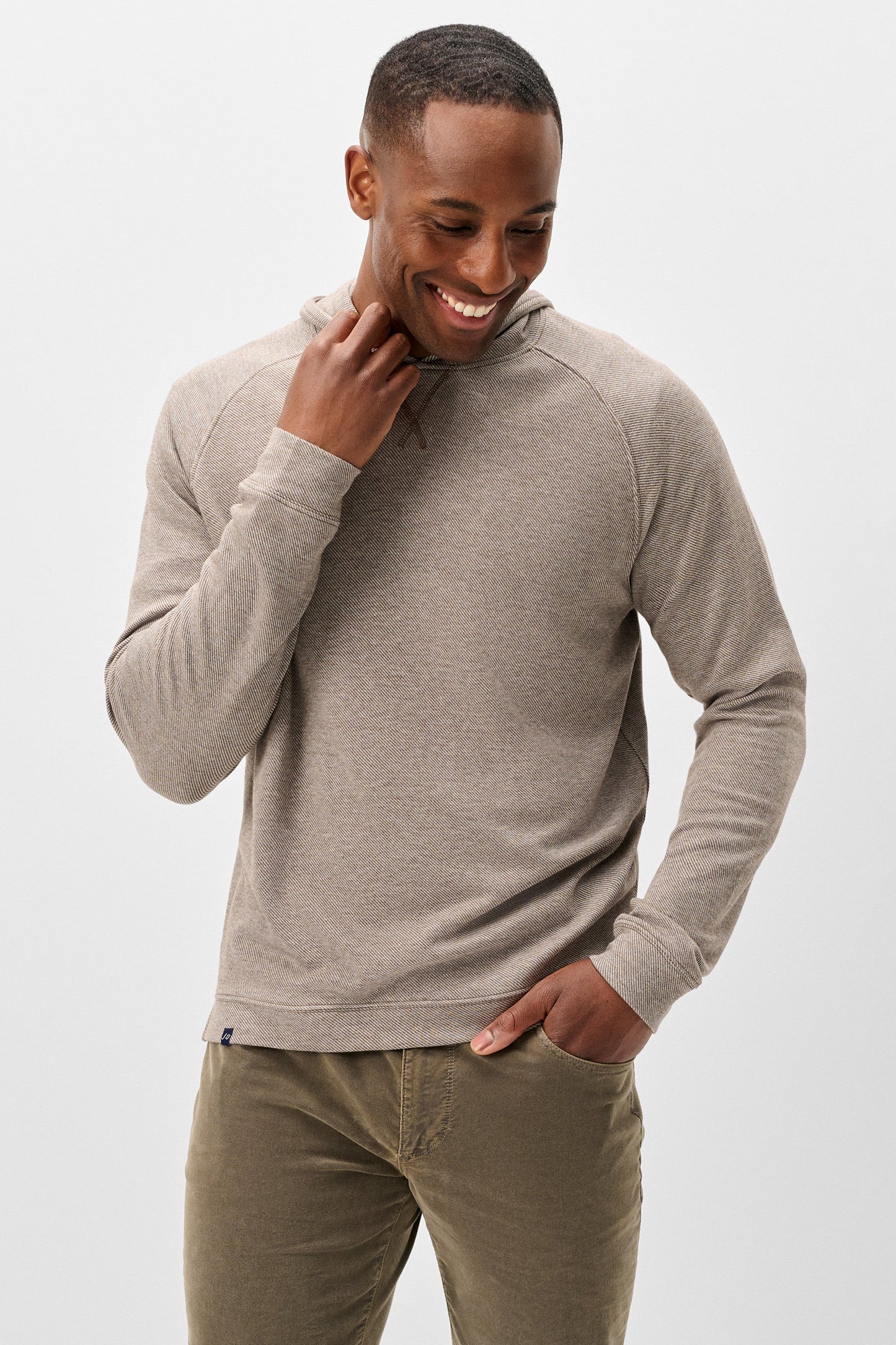 A man wearing a light taupe heathered long-sleeve pullover sweater and olive green pants, standing against a light gray studio background.