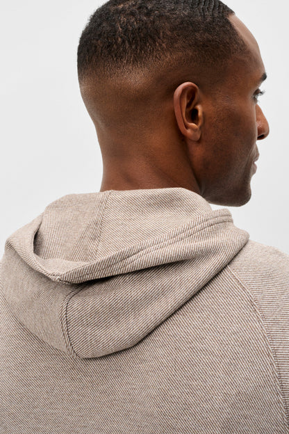 Close-up back and side view of a man wearing a light beige textured hooded sweatshirt against a plain light gray background.