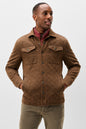 A man wearing a brown diamond-quilted corduroy jacket over a red collared shirt and olive pants, standing against a light gray studio background.