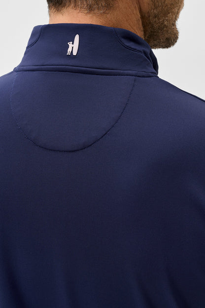 Close-up back view of a man wearing a navy blue high-neck athletic shirt with a small white logo on the collar, against a light gray background.