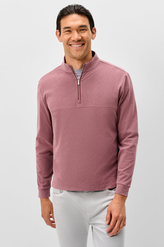 A smiling man wearing a dusty rose quarter-zip long-sleeve knit pullover over a gray undershirt and light gray pants, photographed against a light gray studio background.