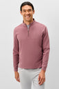 A smiling man wearing a dusty rose quarter-zip long-sleeve knit pullover over a gray undershirt and light gray pants, photographed against a light gray studio background.