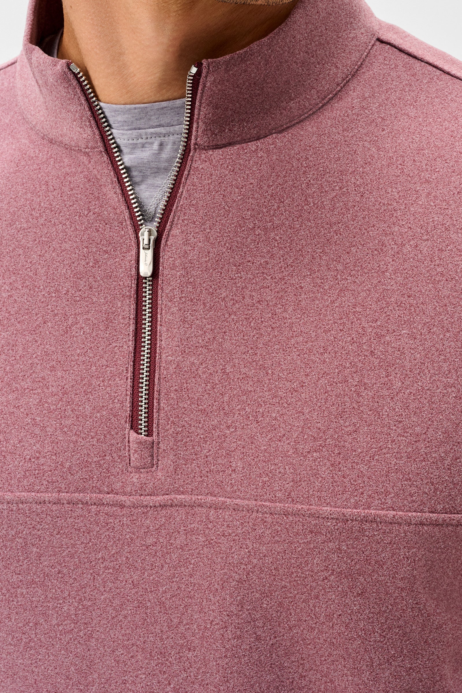 Close-up of a person wearing a heathered dusty rose quarter-zip pullover with a stand collar, showing the zipper, inner gray shirt, and fabric texture.