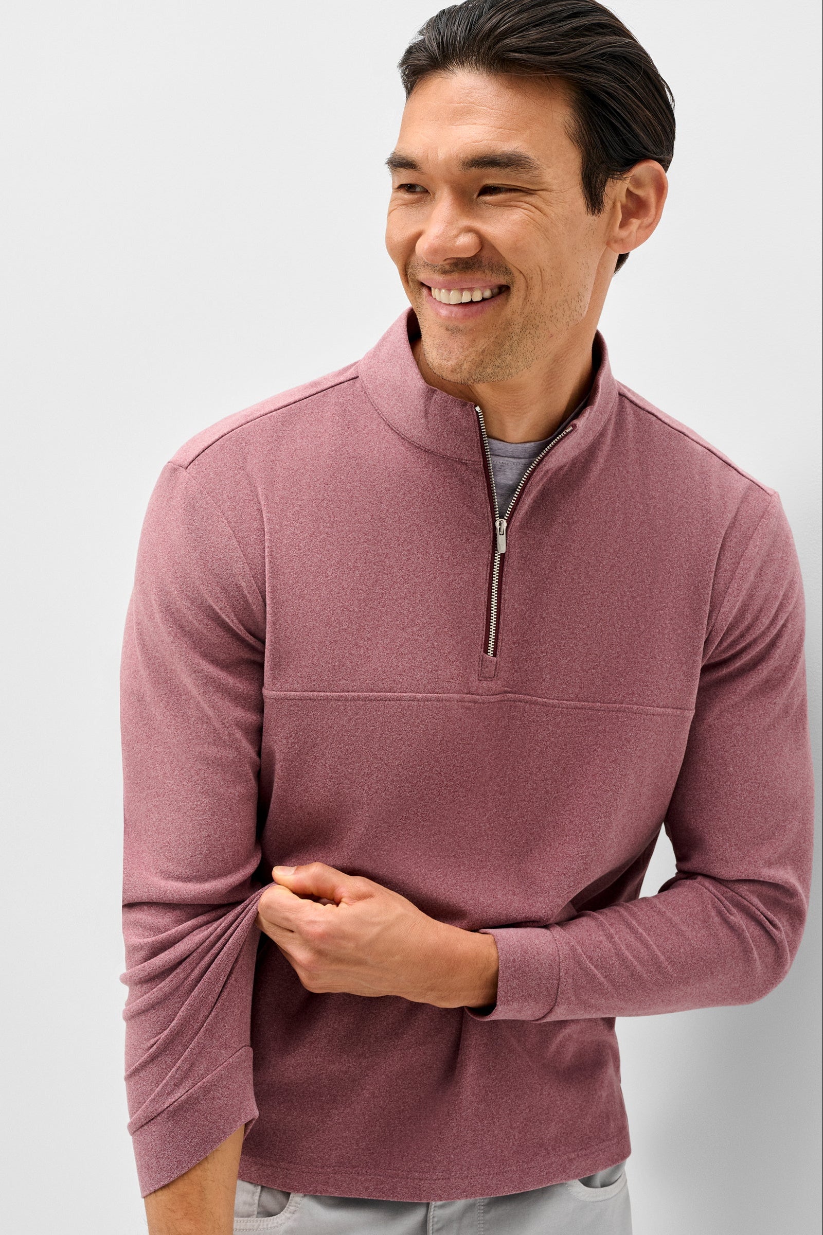 A smiling man wearing a heathered dusty rose quarter-zip long-sleeve pullover over a gray undershirt, shown against a light gray studio background.