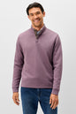 A man wearing a textured, long-sleeve quarter-zip pullover sweater in a dusty mauve-purple color, paired with blue jeans, against a plain light gray studio background.
