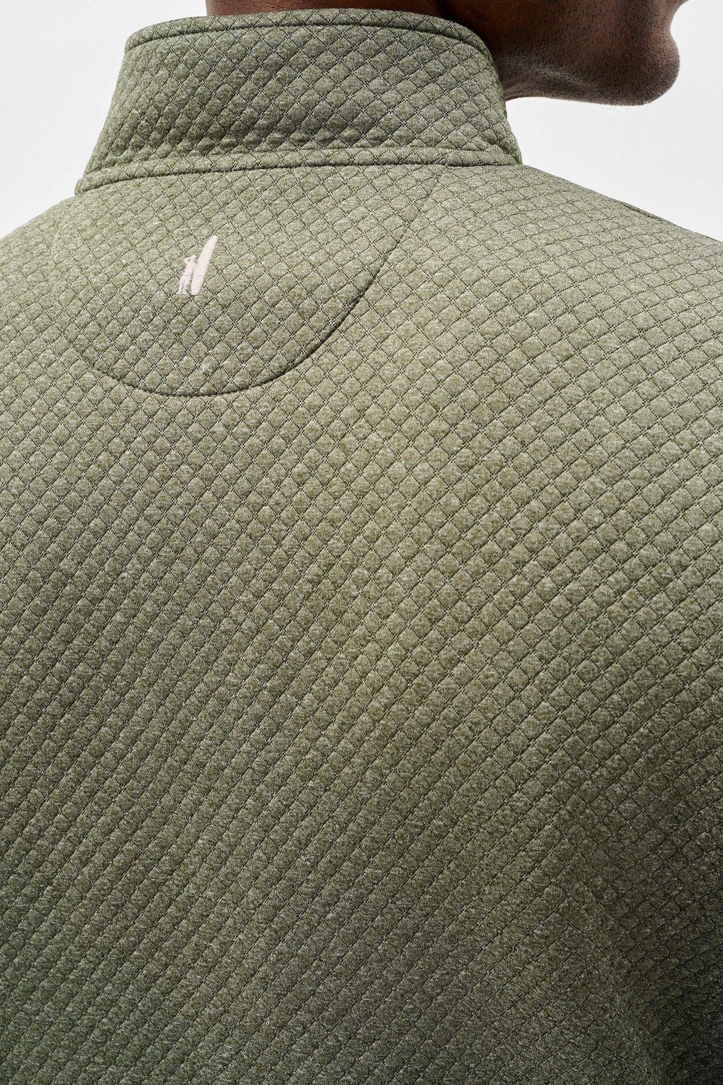 Close-up back view of a person wearing a textured olive green quarter-zip pullover jacket, showing a small white embroidered logo on the upper back.
