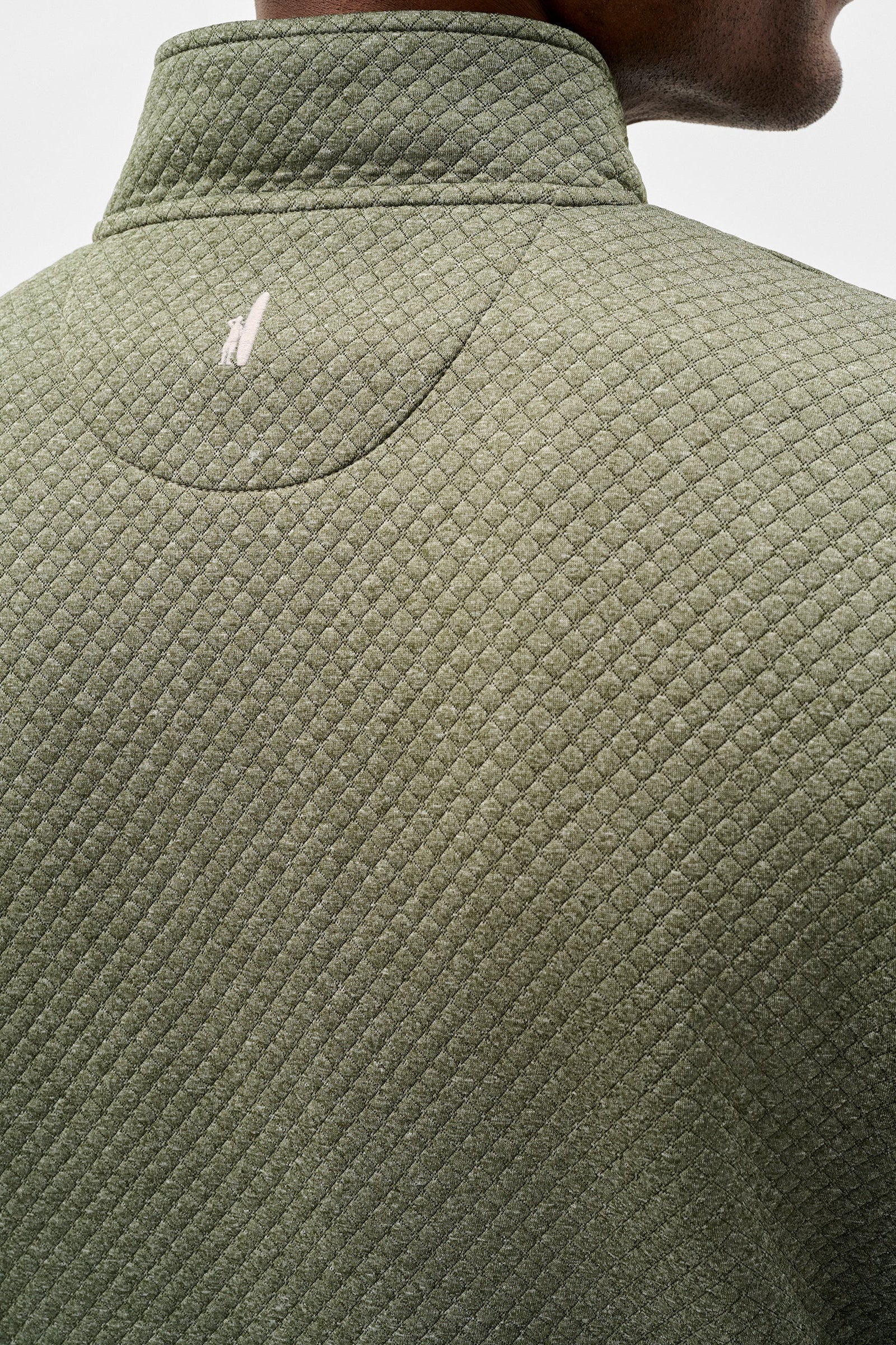 Close-up back view of a person wearing a textured olive green quarter-zip pullover jacket, showing a small white embroidered logo on the upper back.