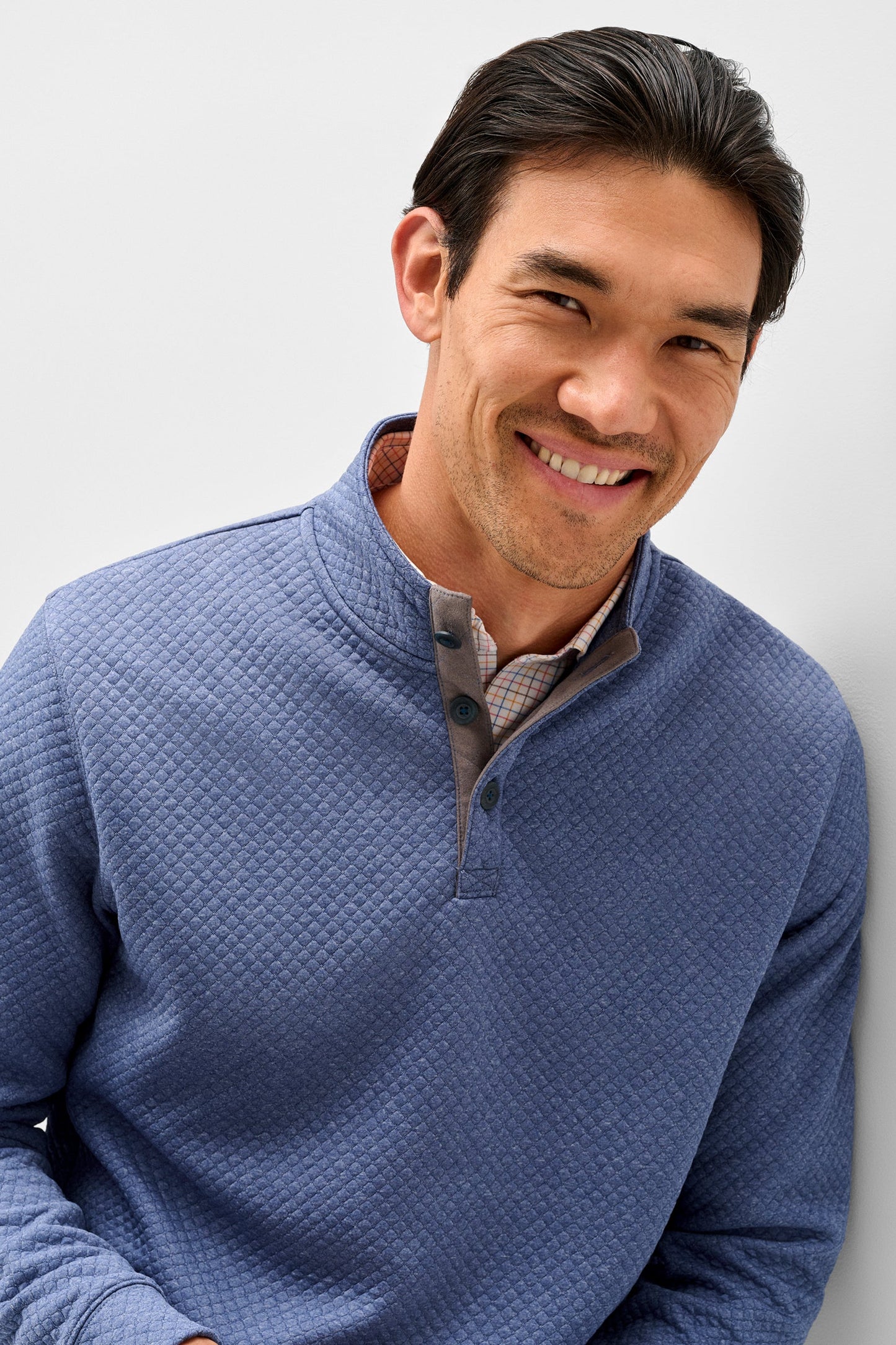 A smiling man wearing a textured blue quarter-zip pullover sweater over a collared shirt, photographed against a clean light gray background.