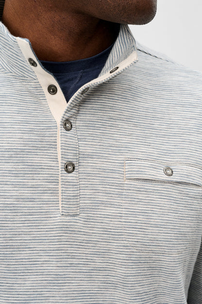 Close-up of a man wearing a light gray and white striped henley shirt with a buttoned collar and a chest pocket, layered over a navy blue t-shirt.