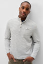 A man wearing a light gray heather long-sleeve henley shirt with a buttoned stand collar and a chest pocket, paired with olive green pants, standing against a light gray background.
