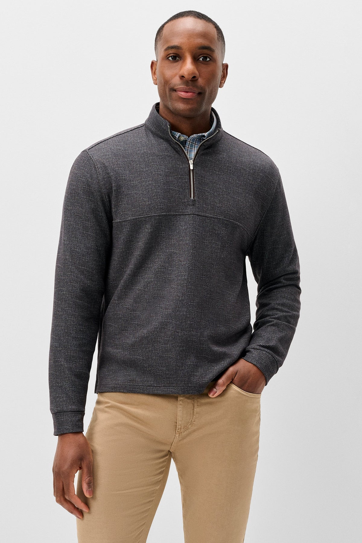 A man wearing a dark gray heathered quarter-zip pullover sweater over a collared shirt and khaki pants, standing against a light gray studio background.