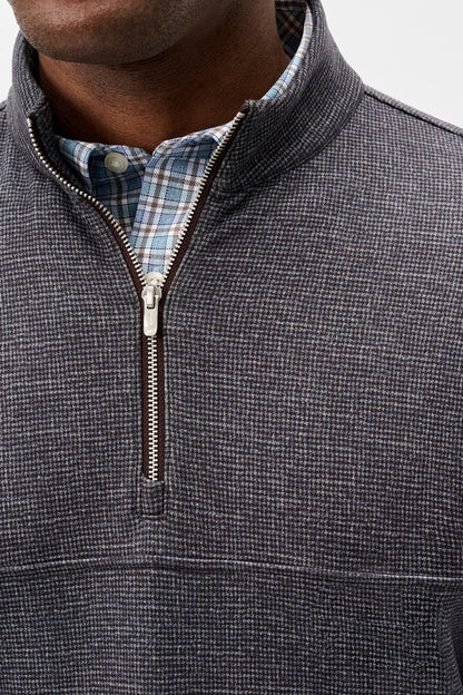 Close-up of a man wearing a charcoal gray textured quarter-zip pullover sweater over a blue and white plaid button-down shirt.