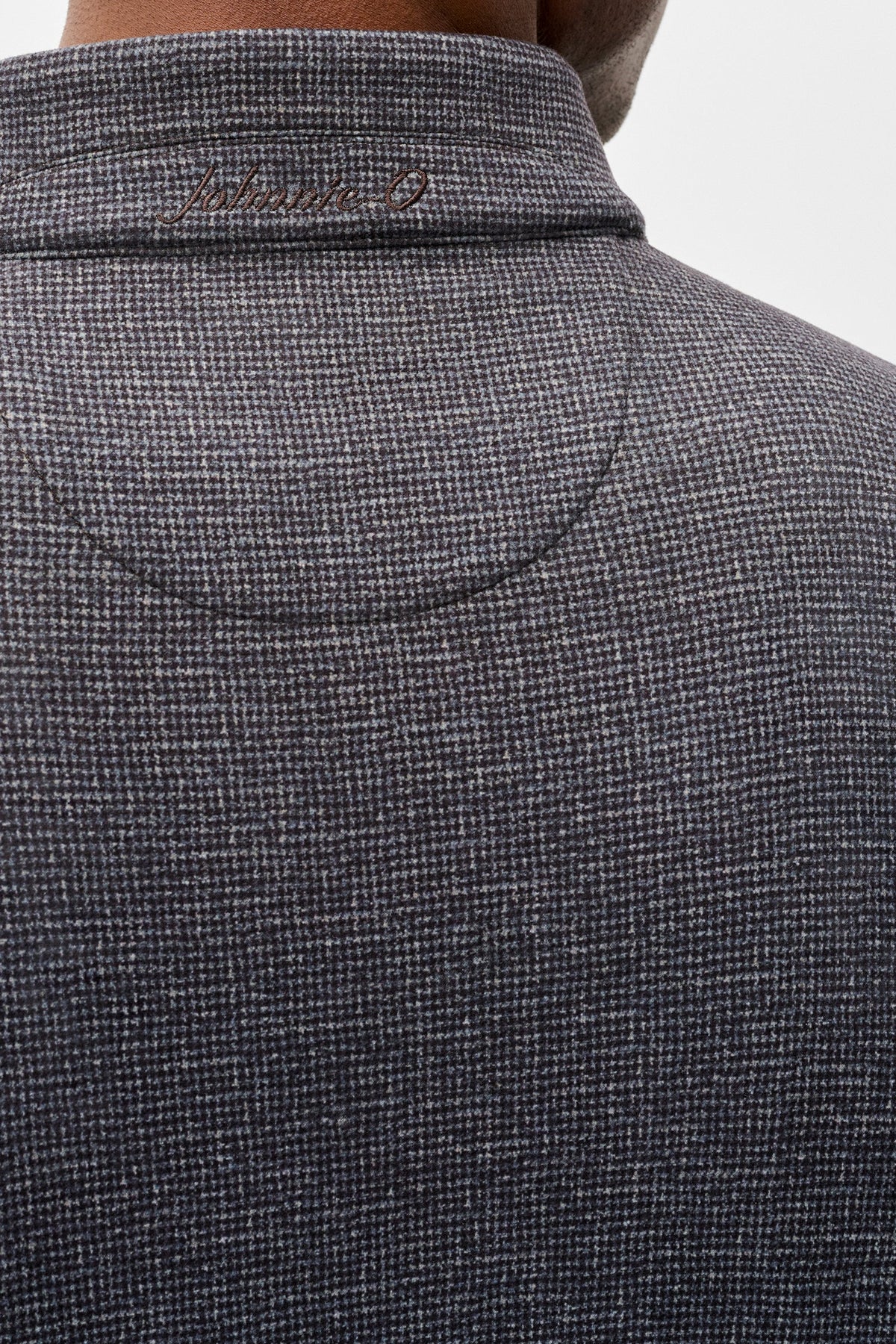 Close-up back view of a person wearing a dark gray textured knit polo shirt with a collar and subtle script embroidery inside the collar.