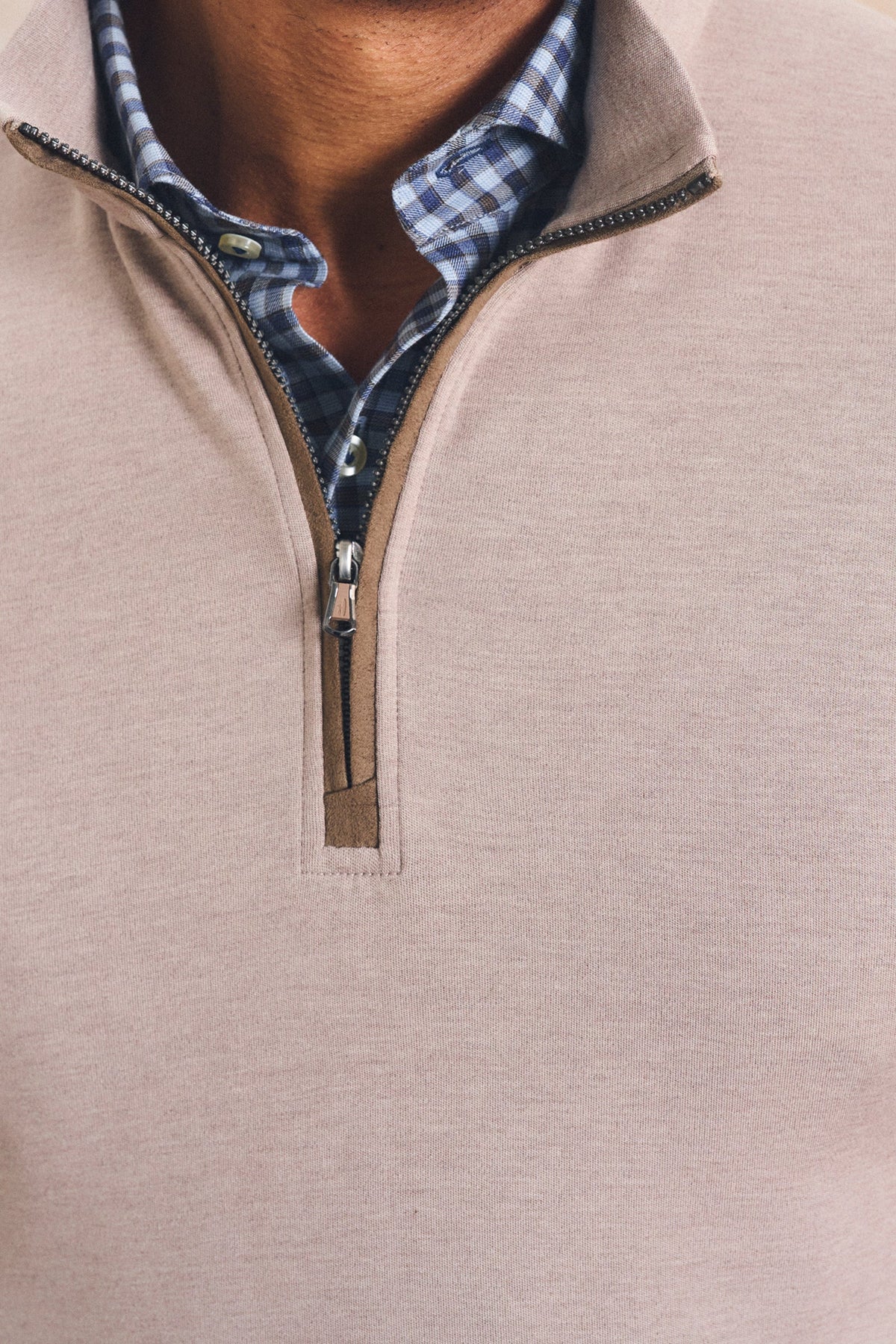 Close-up of a man wearing a light beige quarter-zip pullover sweater over a blue and white checkered shirt.