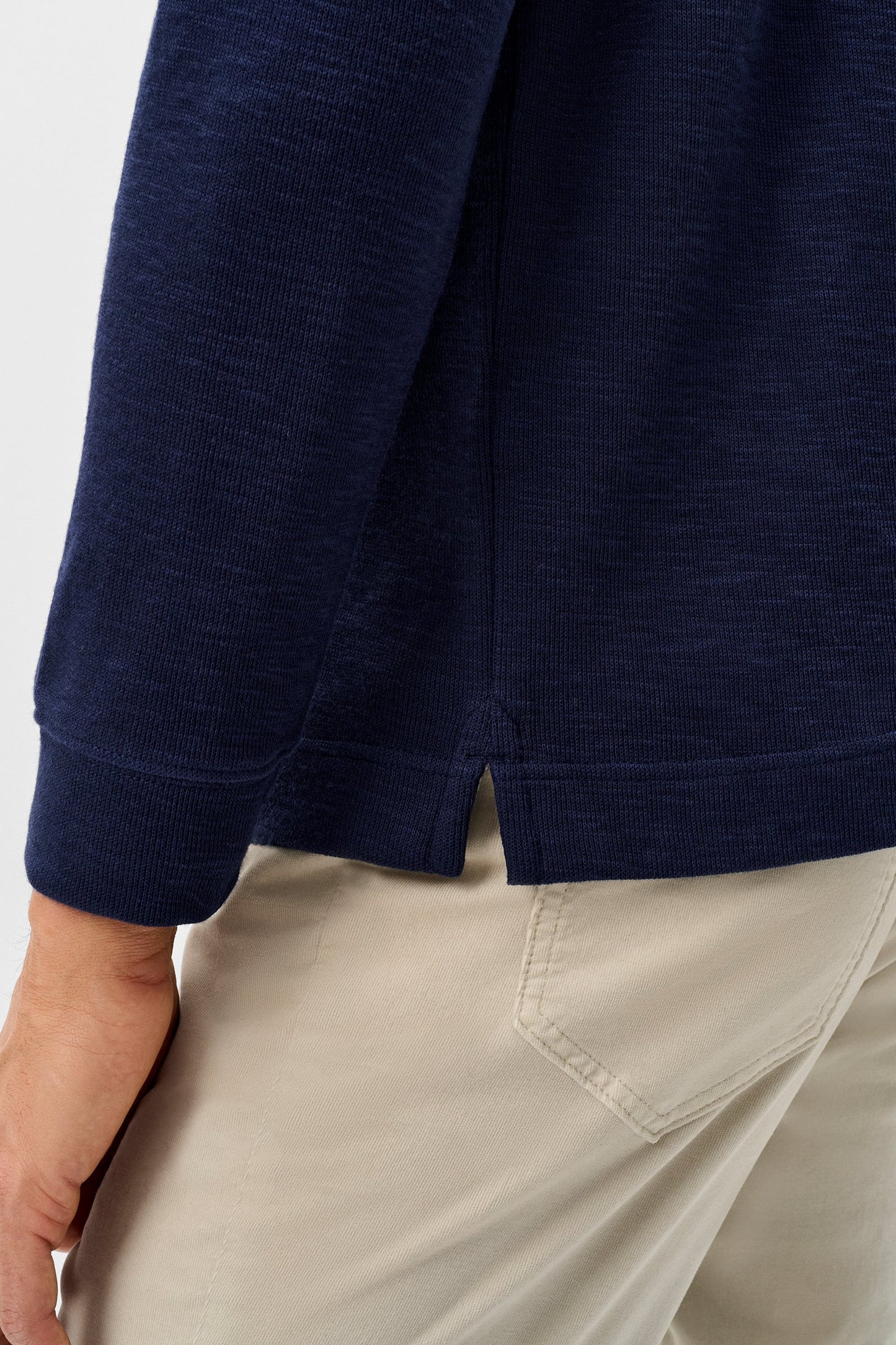 Close-up of a person wearing a navy blue long-sleeve knit top and light beige pants, showing the back cuff and side seam of the top.