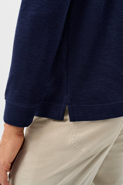 Close-up of a person wearing a navy blue long-sleeve knit top and light beige pants, showing the back cuff and side seam of the top.