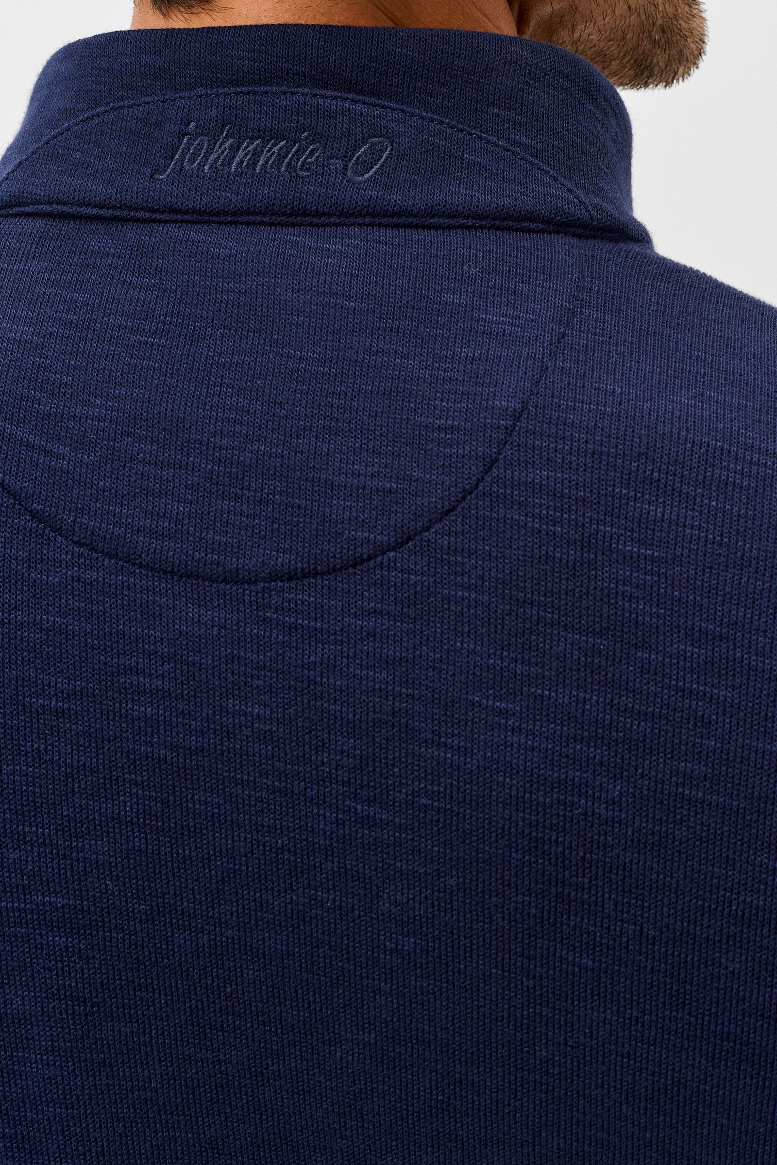 Close-up back view of a person wearing a dark navy ribbed knit quarter-zip pullover sweater, showing the collar with 'johnnie-O' embroidered in gray.