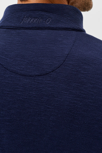 Close-up back view of a person wearing a dark navy ribbed knit quarter-zip pullover sweater, showing the collar with 'johnnie-O' embroidered in gray.