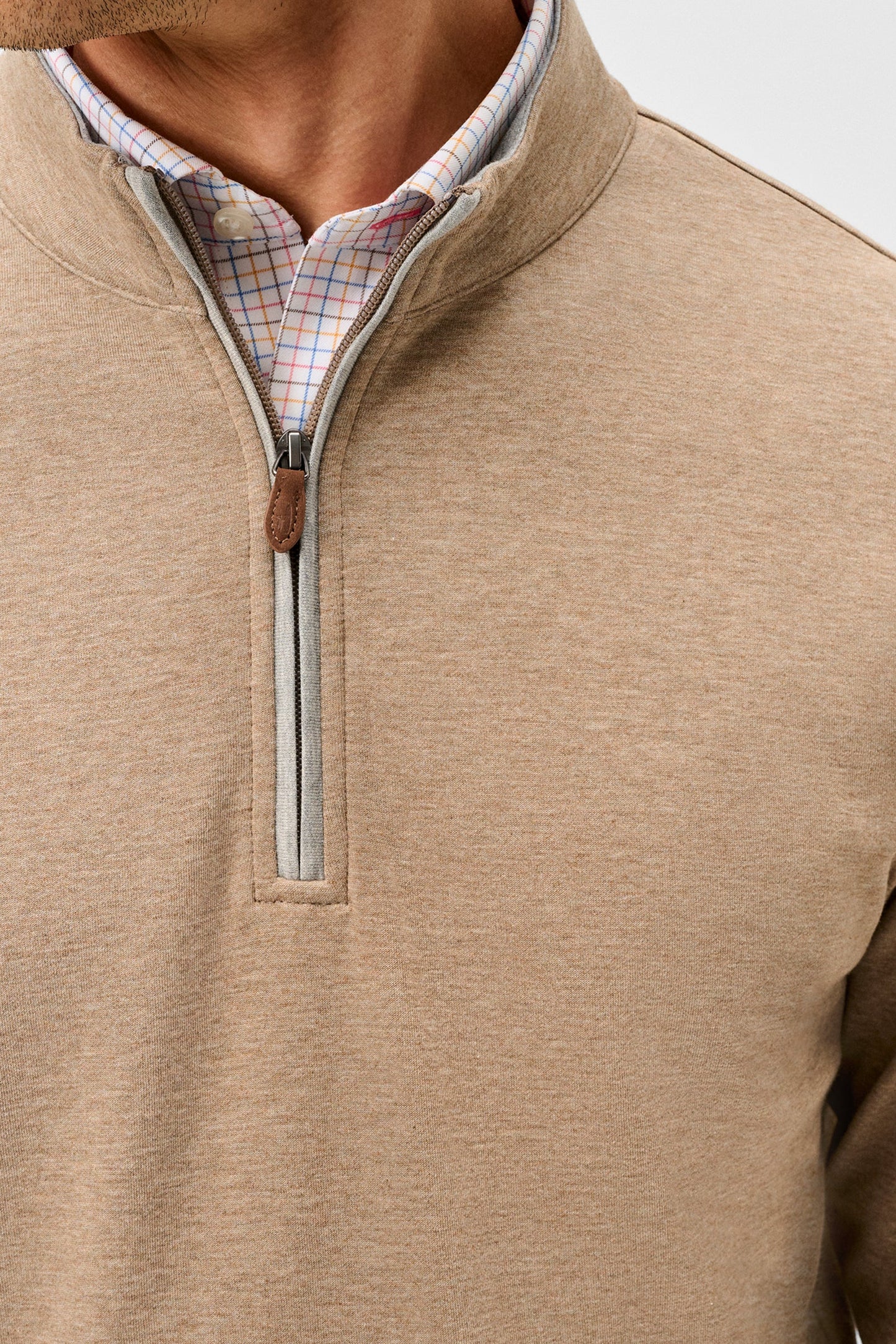 Close-up of a man wearing a beige quarter-zip pullover sweater over a plaid collared shirt, showing the collar, zipper, and chest area.