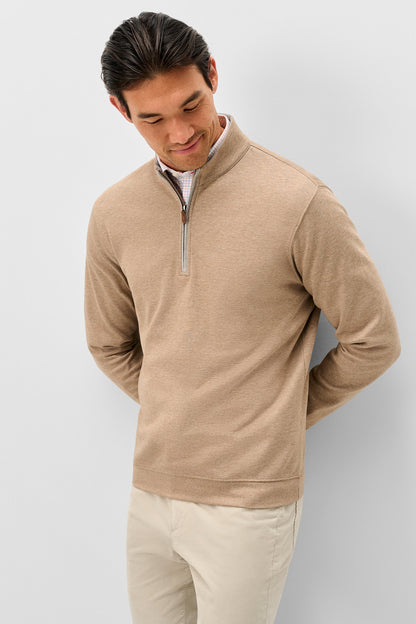 A man wearing a beige quarter-zip pullover sweater and light beige pants, standing against a light gray studio background.
