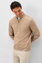 A man wearing a beige quarter-zip pullover sweater and light beige pants, standing against a light gray studio background.