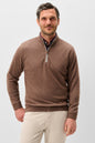 A man wearing a brown quarter-zip knit sweater over a patterned collared shirt and beige trousers, photographed against a light gray studio background.